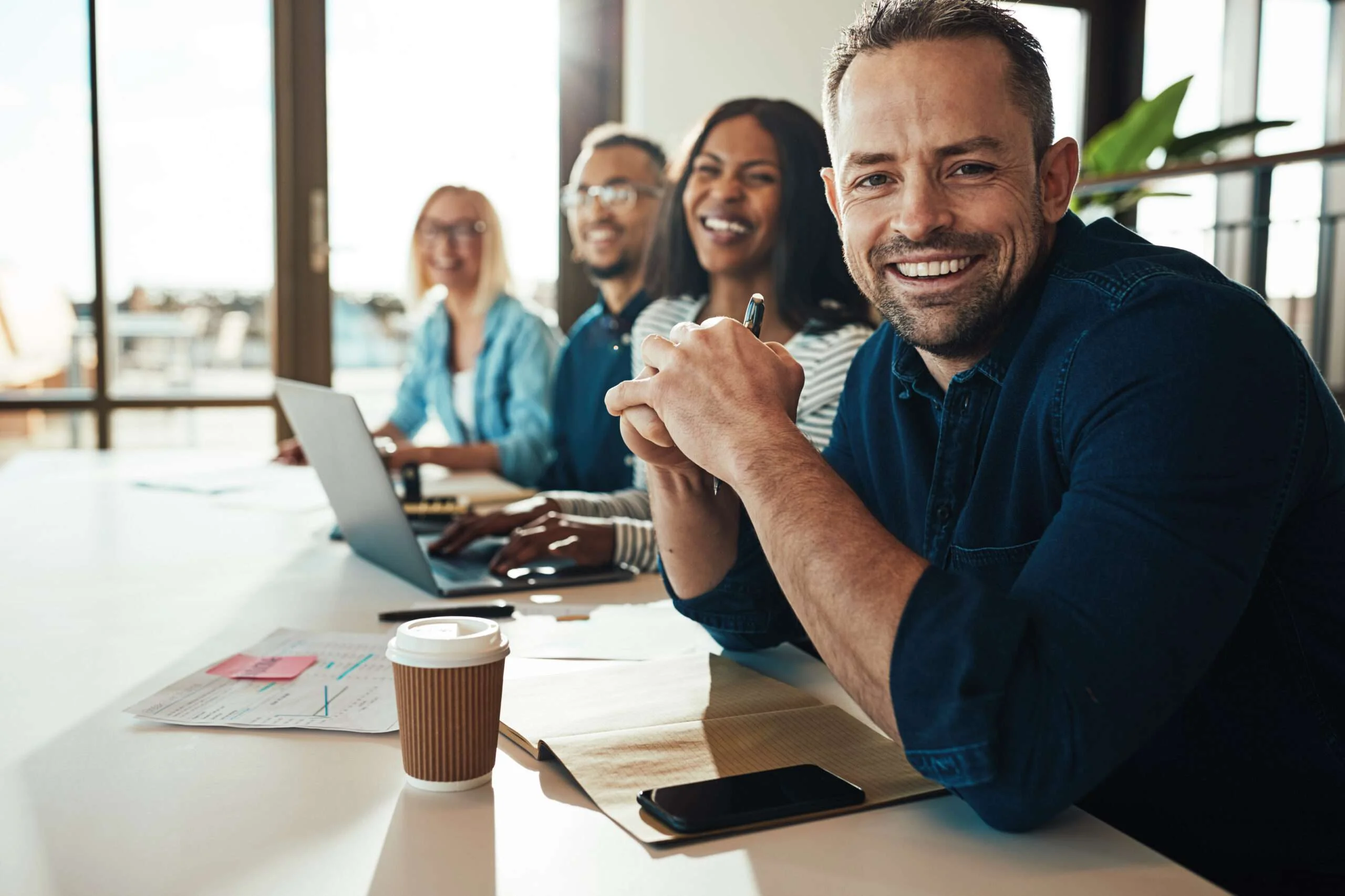 Smiling businessman sitting with a diverse group of coworkers during a meeting together at a table in an office